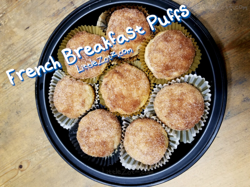 a photo of a black storage container/tupperware filled with several French breakfast puffs. the cinnamon sugar muffins are on display on a wooden tabletop
